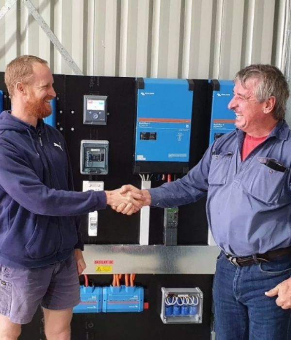 Photo of two men shaking hands in front of a solar battery system