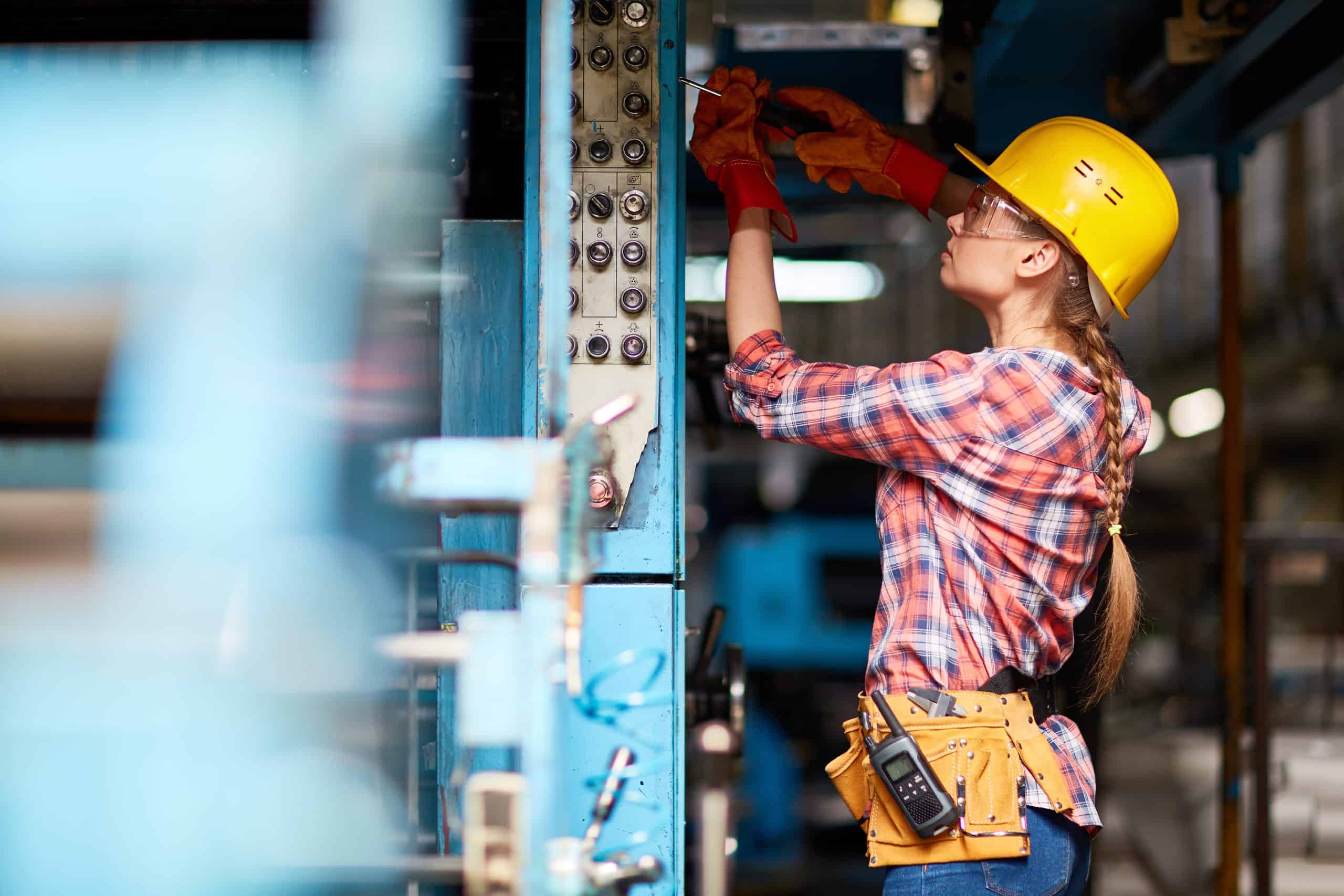 Female electrician with screwdriver repairing machine at plant