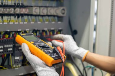 Electrician engineer uses a multimeter to test the electrical installation and power line current in an electrical system control cabinet.